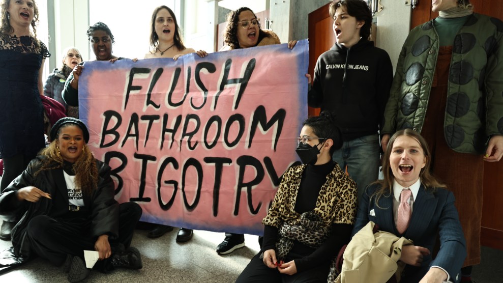 A pink poster says "Flush Bathroom Bigotry" held up by protesters standing and seated.