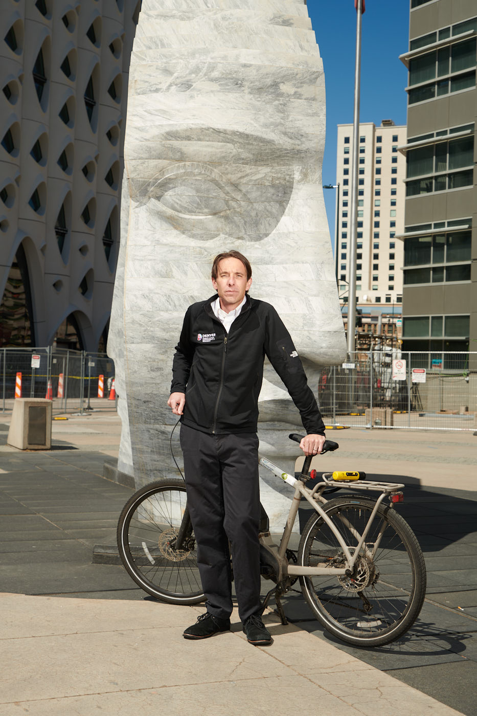 Man standing with a bicycle in front of a stone statue.