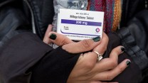 A close-up photo of a person's hands, holding a box containing one 200 mg mifepristone tablet.