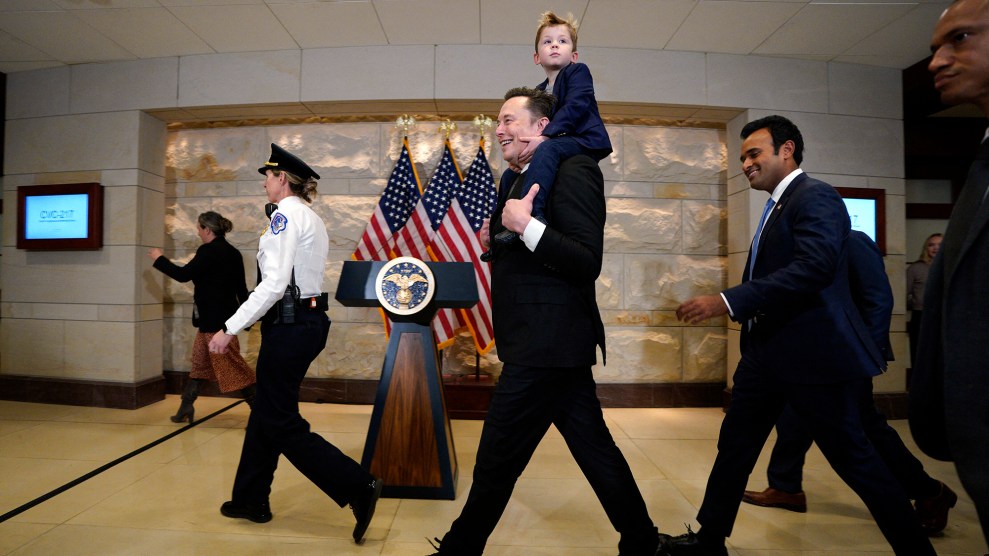 A white man holds a white boy. Both are wearing suits. In front of them a security guard, and behind them an Indian man wearing a suit.