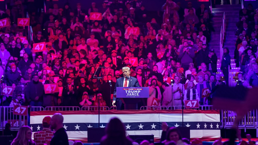 Donald Trump stands on a podium in front of a stadium of people.