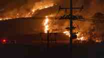 A transmission line is silhouetted by burning hills.