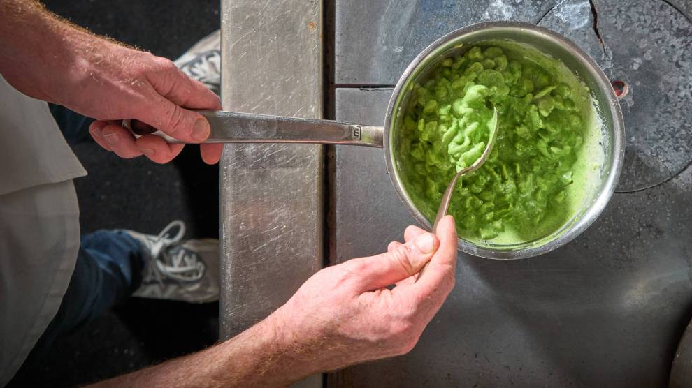 Two white hands stir a pot with a green substance inside.