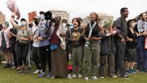 A line of students links arms at a protest. One speaks into a bullhorn.