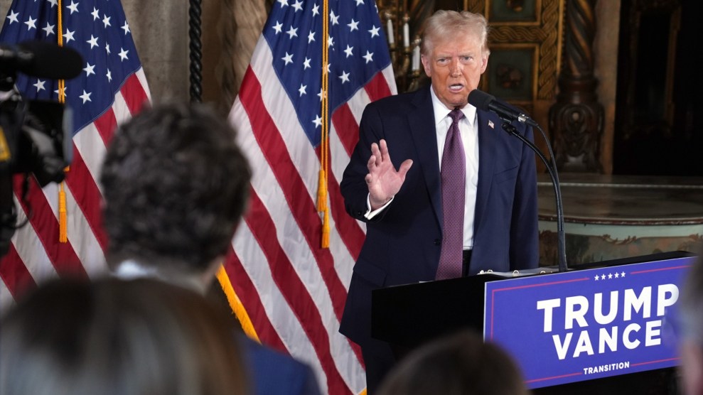 Donald Trump speaks to an audience from a dais in front of an American flag.