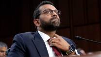 Kash Patel loosening his tie and seated in front of a microphone