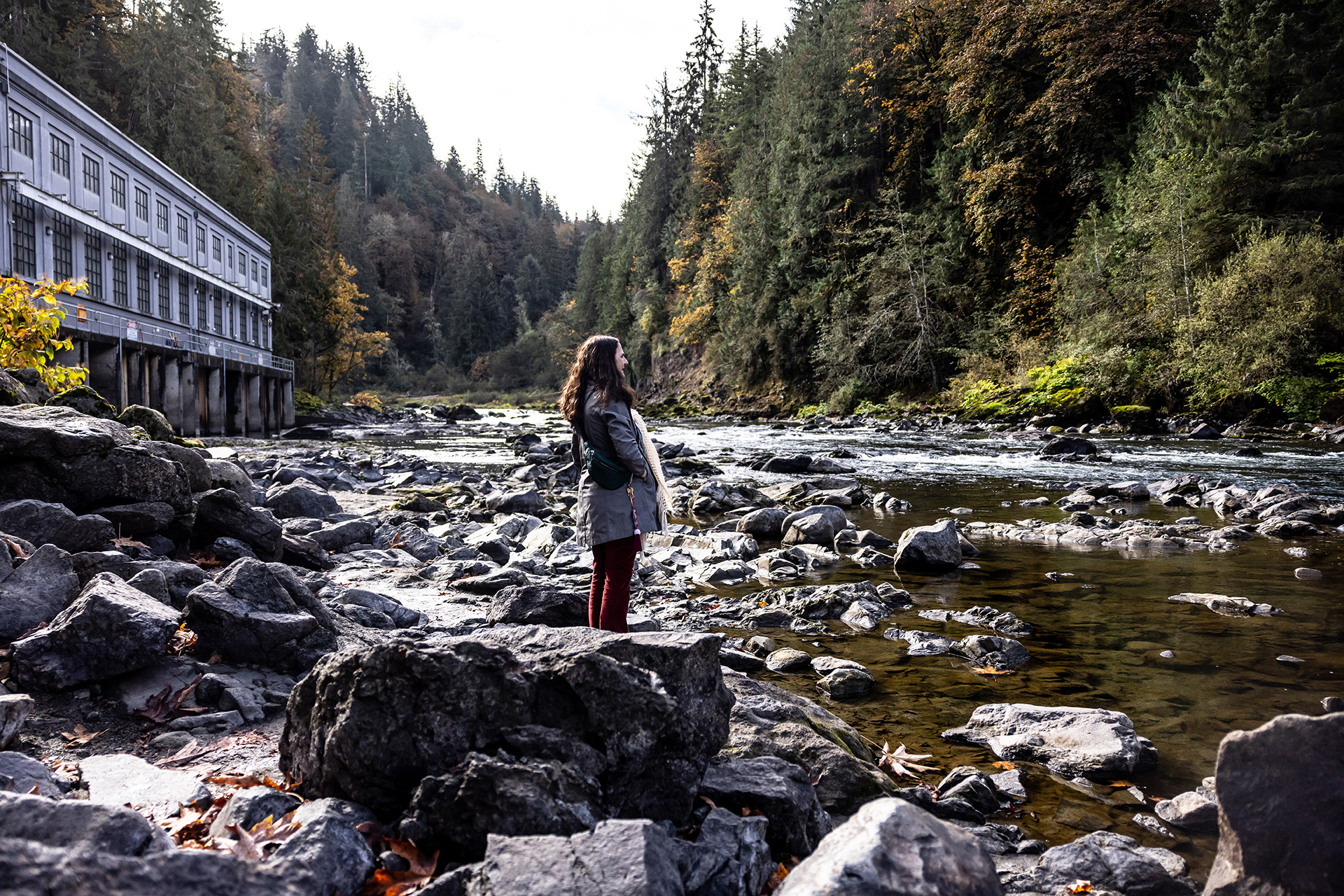 Woman standing on the edge of a river with big rocks around her.