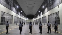 Six uniformed men stand in a row in a wide hallway between holding cells.