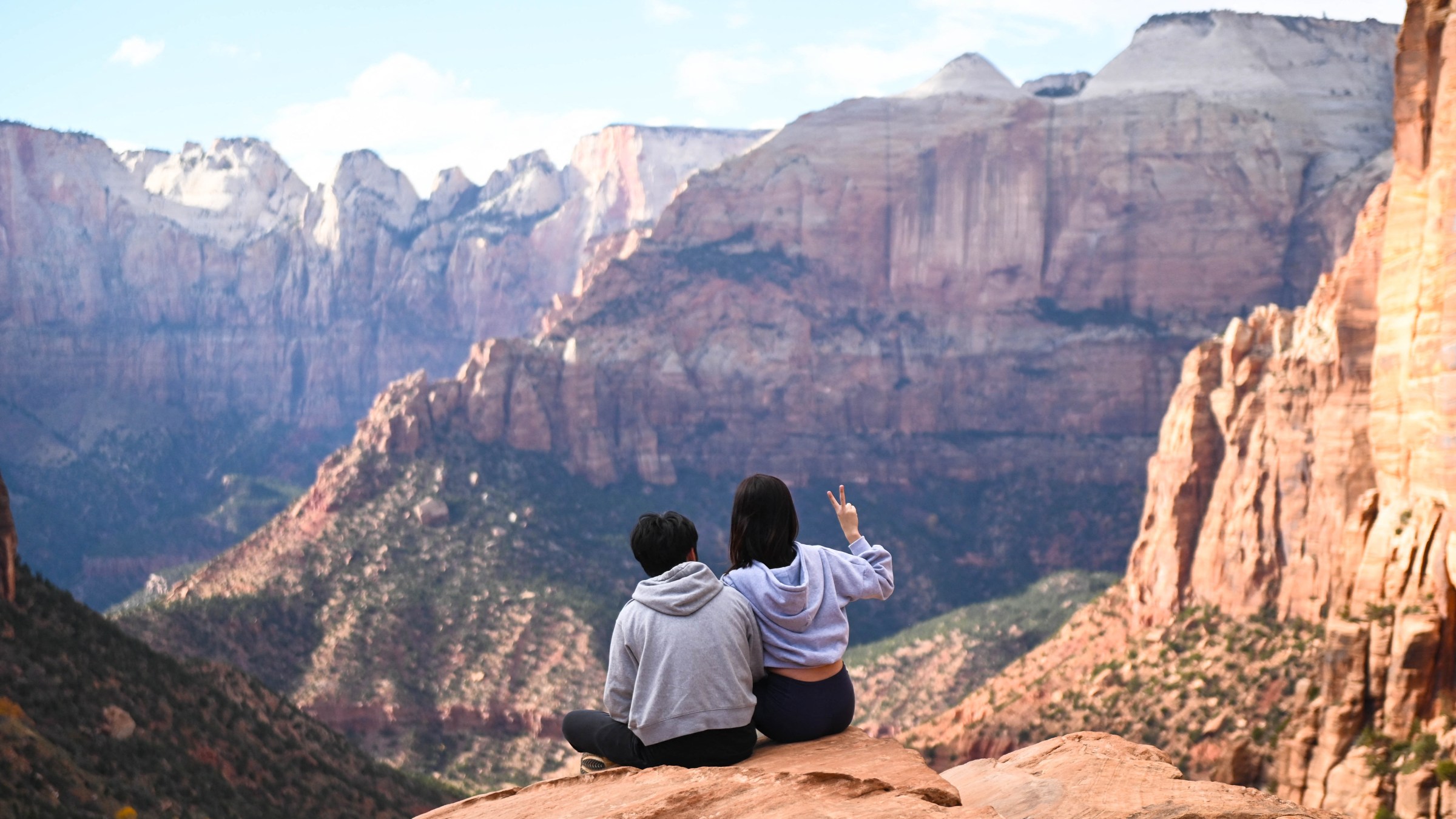 Two hikers sit on a rock and look at a vast landscape.