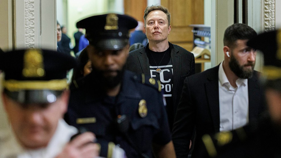 A white man stands behind a crowd of officers. He wears a black T-shirt and a suit jacket.