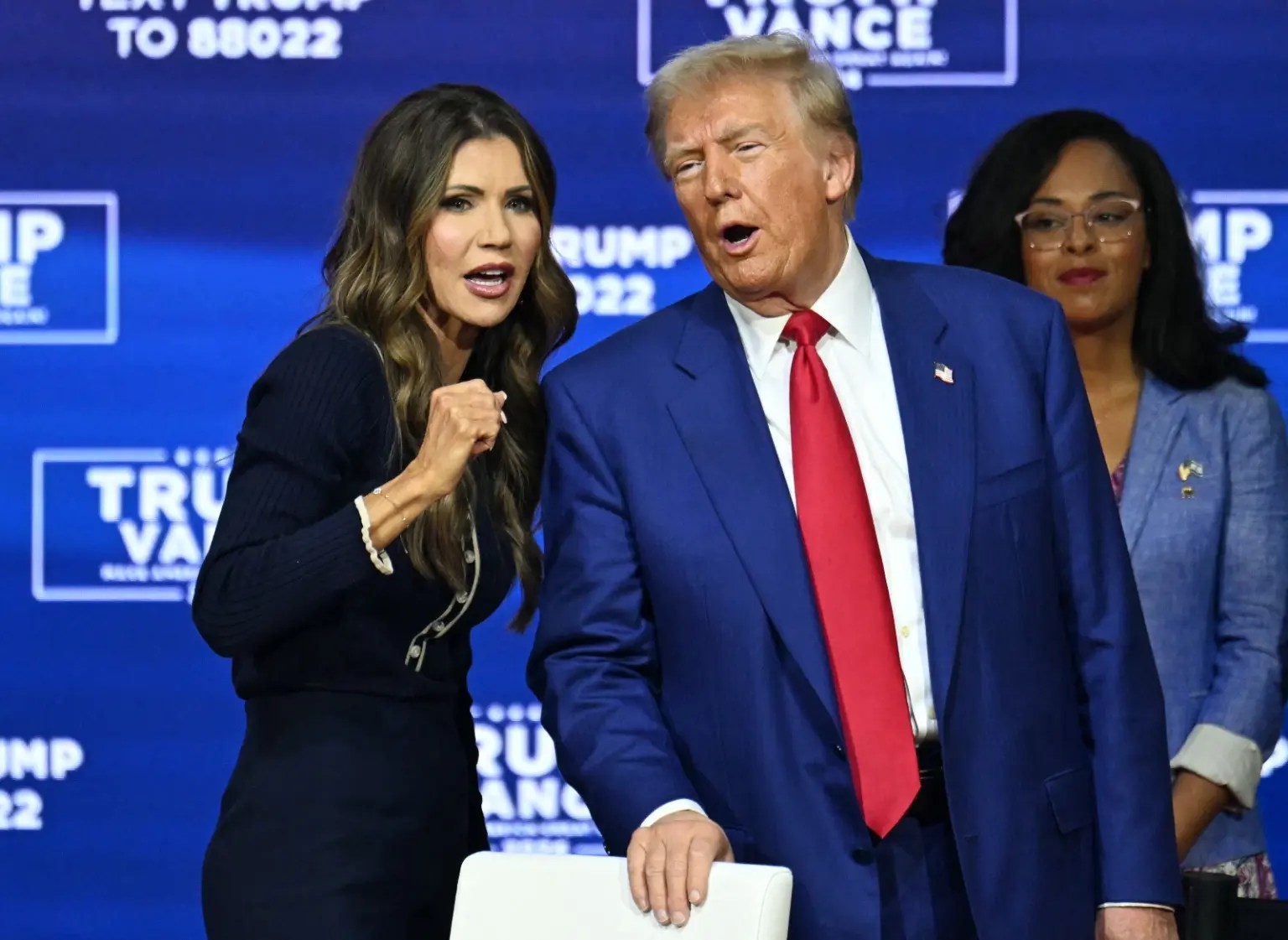 A white man and a white woman stand in front of a "Trump Vance" wall.