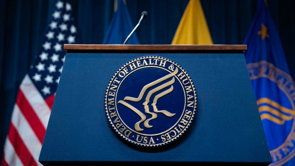 A podium which says "Health and Human Services" on it. There are four flags, including an American flag, in the background.