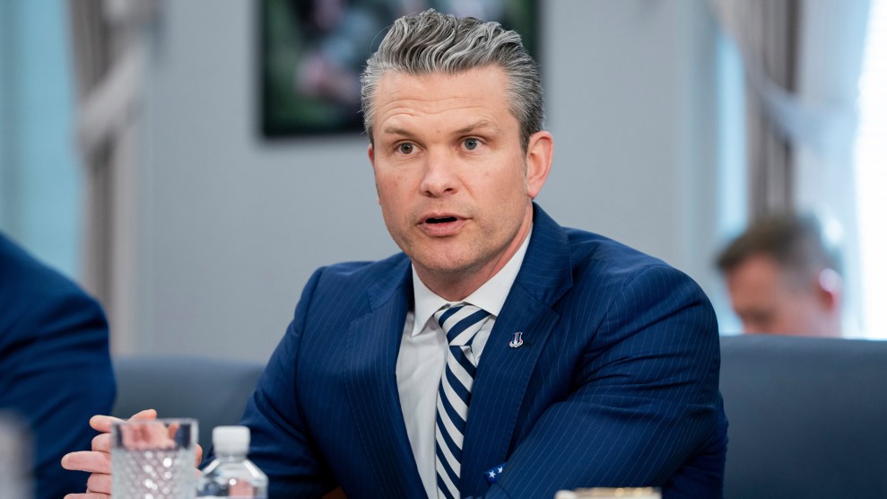 A white man with graying hair wearing a blue suit jacket and striped tie, who appears to be speaking and sitting in an office.