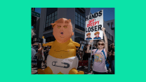 A horizontal photo of protestors on a bright green background. In the photo, a woman in a pink shirt and sunglasses holds a sign that reads "HANDS OFF! CREEPY LOSER.' To the left of the protestor is an inflatable balloon of Donald Trump charactered as a baby. The baby is shirtless, but wears a diaper. Trump, as the baby, appears to be crying.