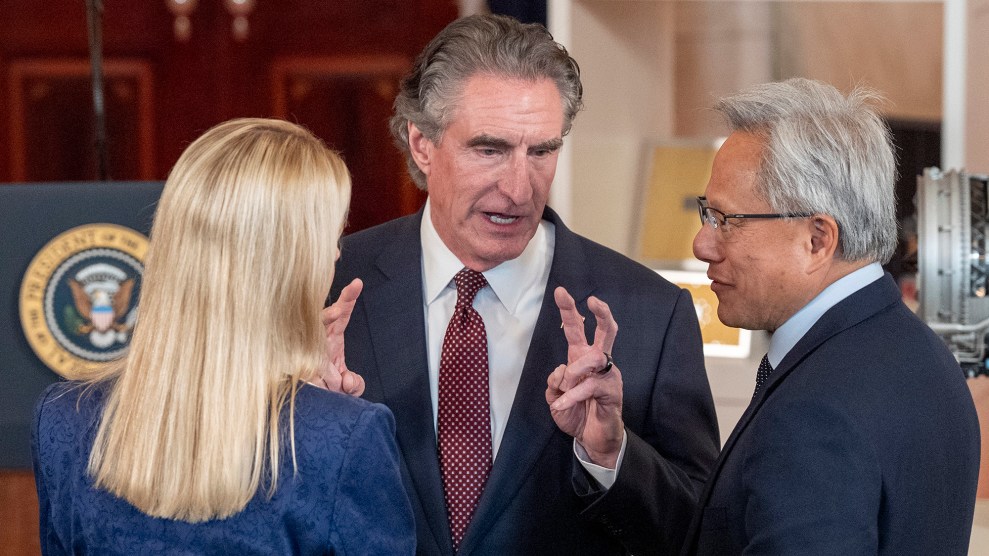 A white man with slick back hair holds his fingers in the quotation mark position.