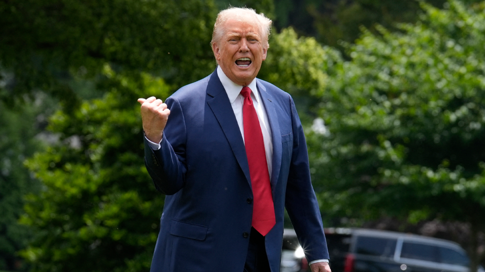 Donald Trump, in suit and tie while outdoors, yells in the direction of the camera while using his thumb to point at something over his right shoulder.