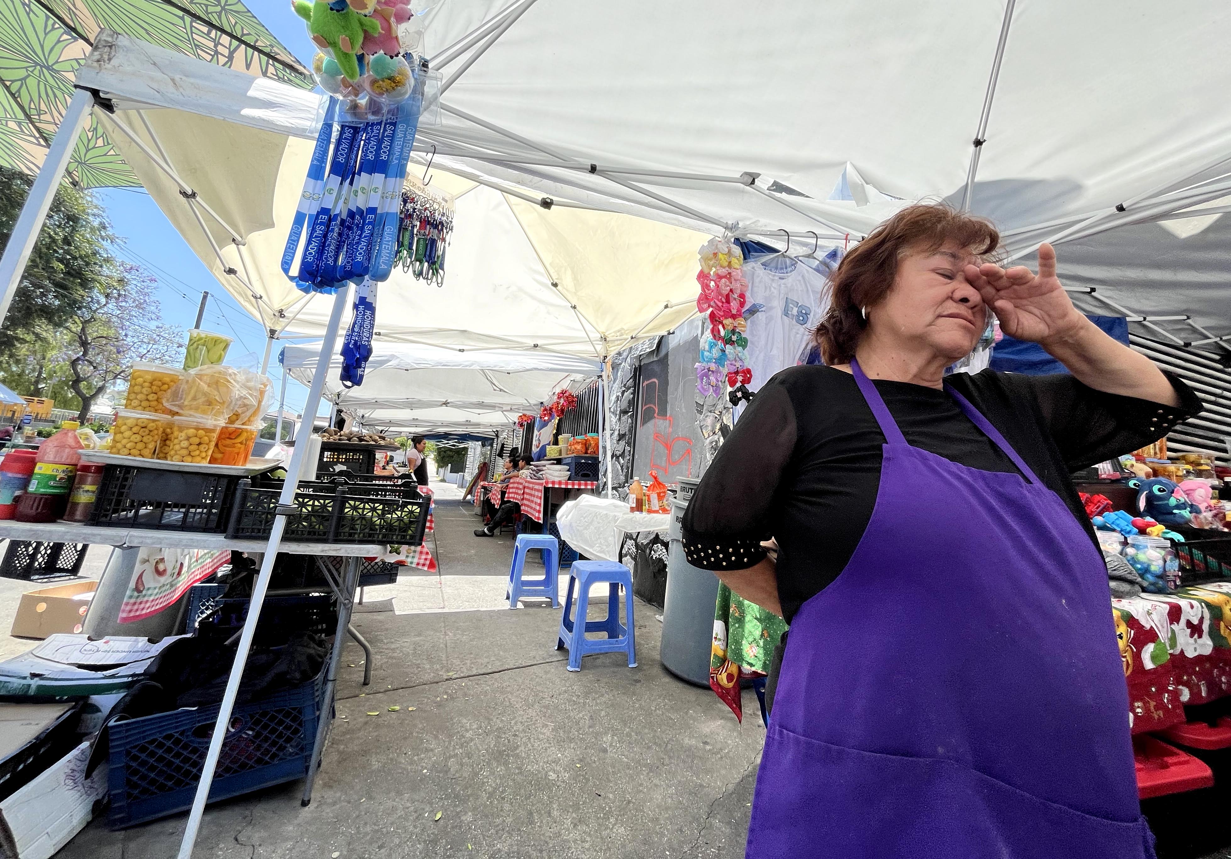 A woman is touching her face under a white canopy surrounded by different vending booths.