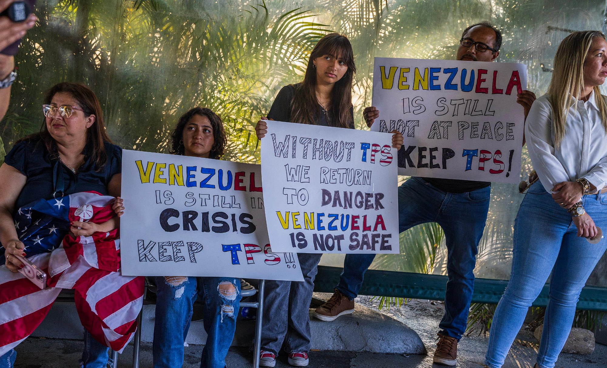 Five people gathered, three of them holding signs in support of TPS program.