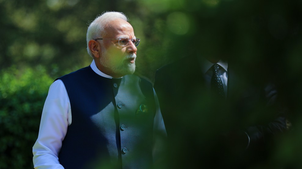 Indian Prime Minister Narendra Modi looks off to the side as he stands in a garden. The shot is partially obscured by out-of-focus leaves in the foreground.