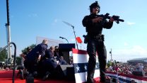 A countersniper stands on the stage at the site of the first assassination attempt of Trump in Butler, Pennsylvania, while several Secret Service Agents crouch on the stage to protect the president.