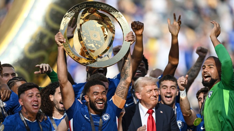 Smiling soccer players in blue jerseys on a sunny day hold a golden club world cup trophy aloft as Donald Trump embarrasses himself by crashing their party