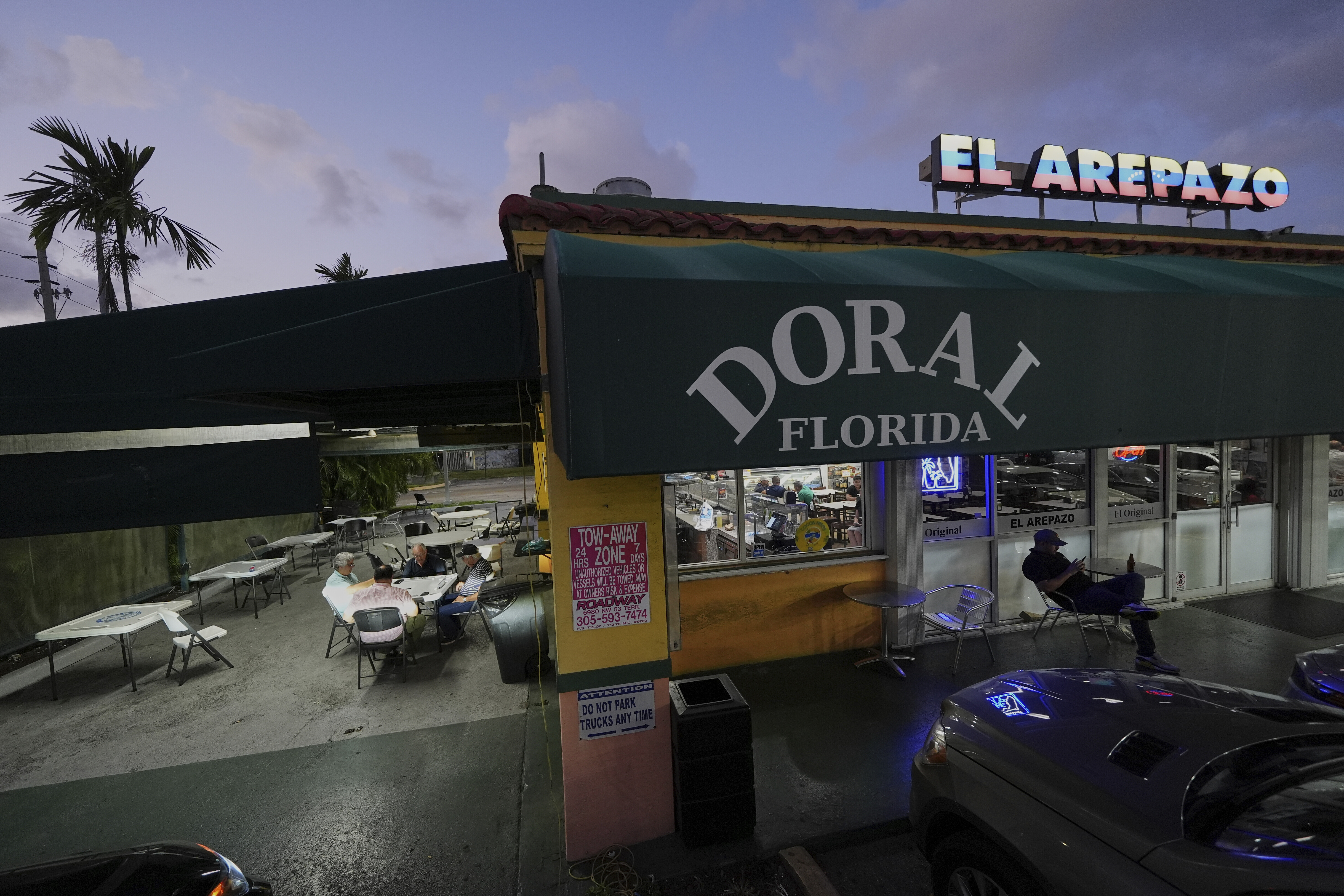 Dusk outside a a Venezuelan restaurant, with a man sitting out front in a chair.