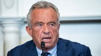 Close up image of Robert F. Kennedy Jr. speaking into a small microphone. He is wearing a suit and looking towards the side of the frame.