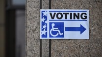 A sign with a wheelchair that says voting on it pointing towards accessible voting.