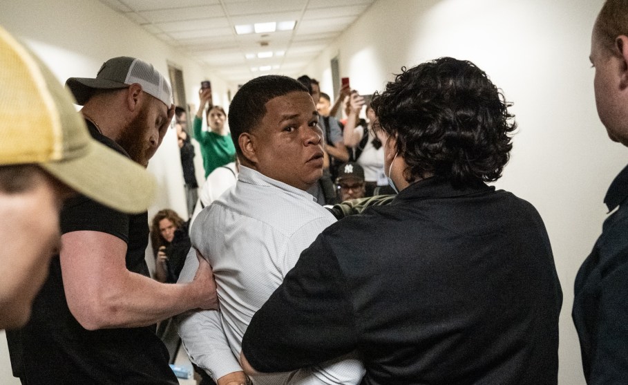 Two ICE agents escort a handcuffed man down a crowded hallway, after detaining him when he exited an immigration hearing.