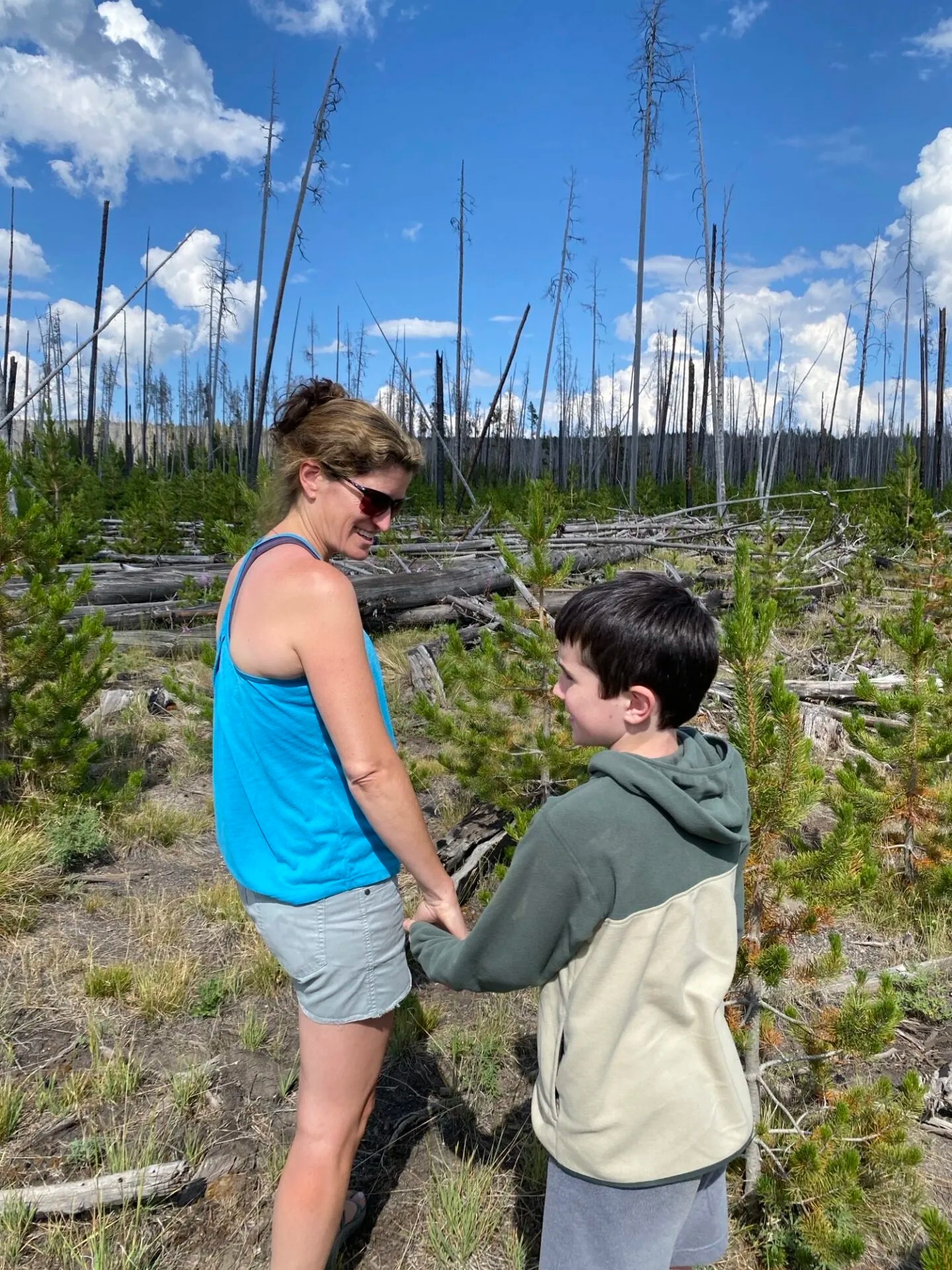 A mom and her son hold hands and walk through a forest.