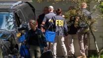 FBI agents with agency jackets stand in a driveway