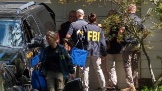 FBI agents with agency jackets stand in a driveway