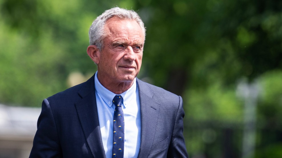 RFK Jr, a white man, in a blue suit walking outside near trees