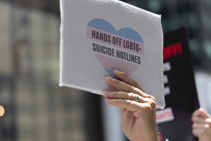 A sign with a heart in trans flag colors which says "hands off LGBTQ+ suicide hotlines."
