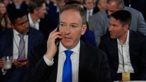 A white man in a dark jacket and bright blue tie speaks on a cellphone as he waits for President Trump to speak at an event.