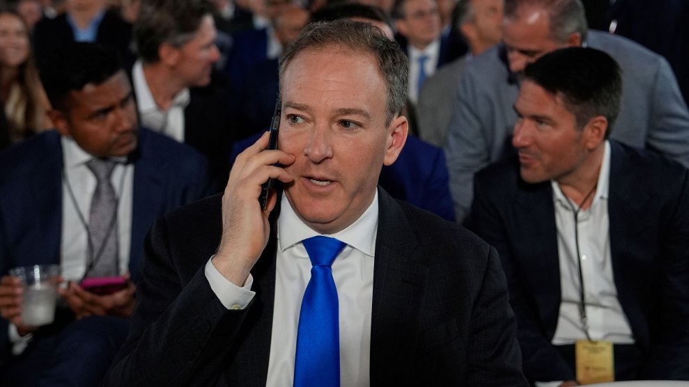 A white man in a dark jacket and bright blue tie speaks on a cellphone as he waits for President Trump to speak at an event.