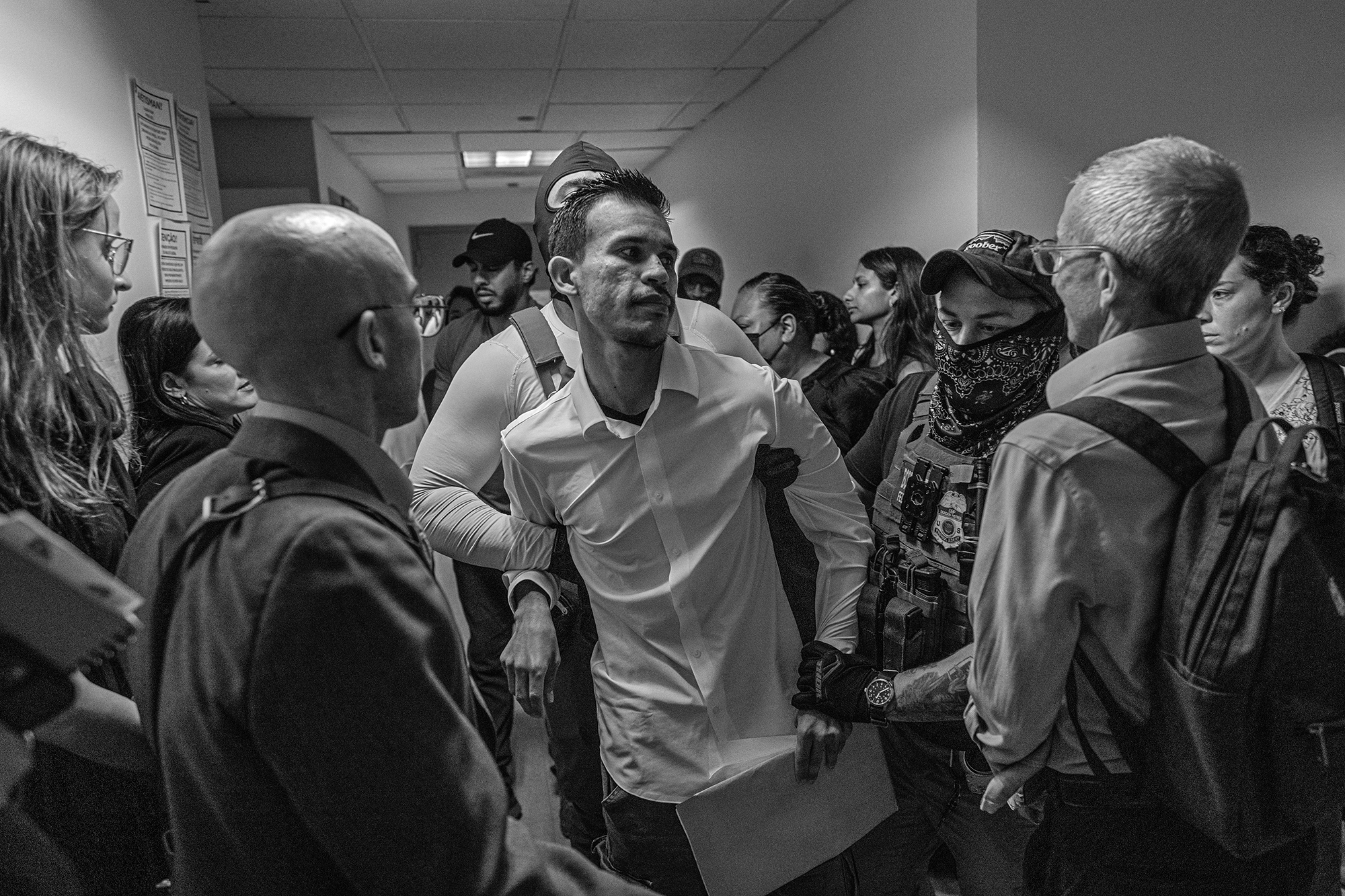 Group of people surround ICE agents detaining a man outside a courtroom.