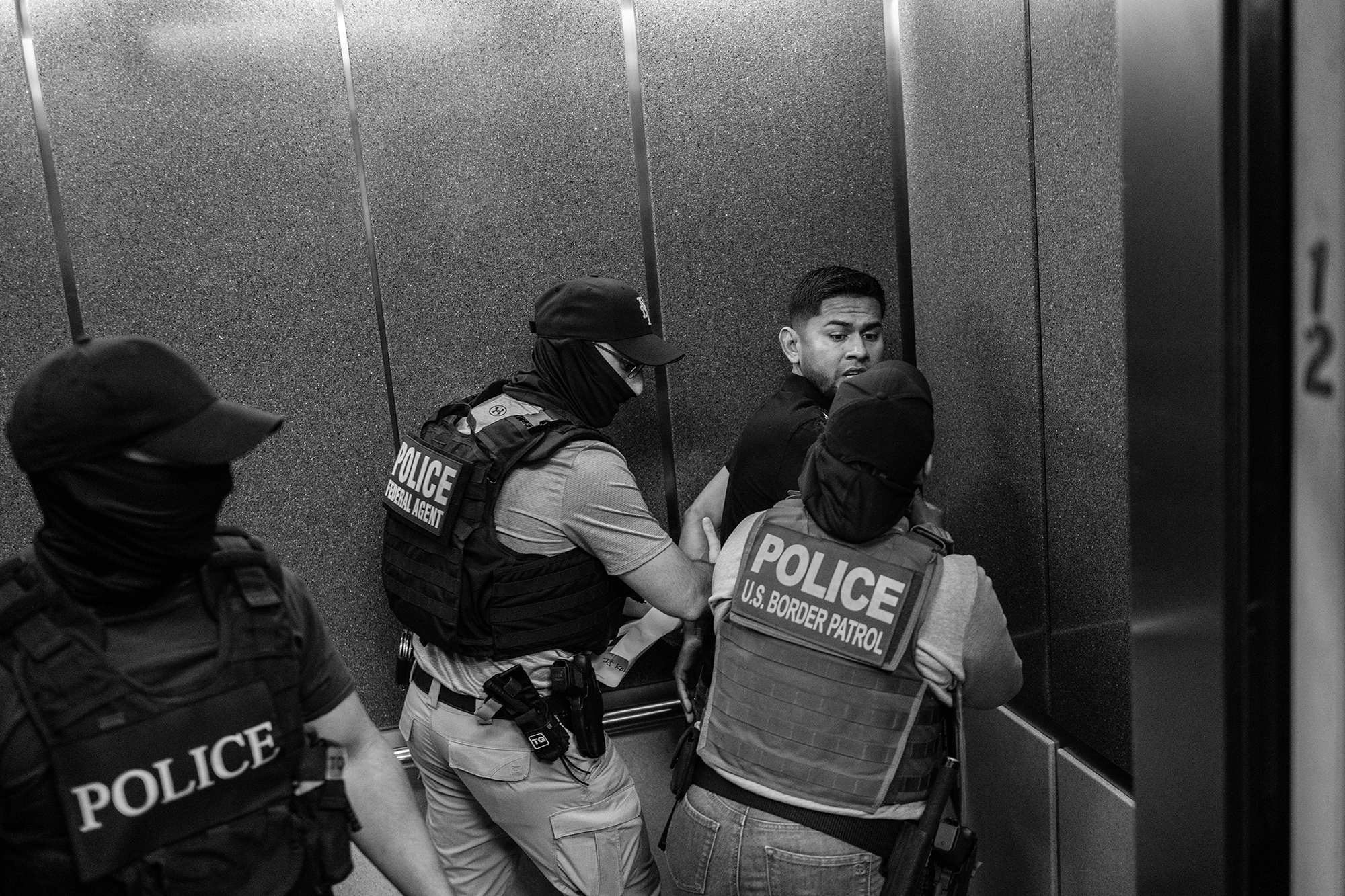 Federal agents press a man against a corner of an elevator as they detain him.