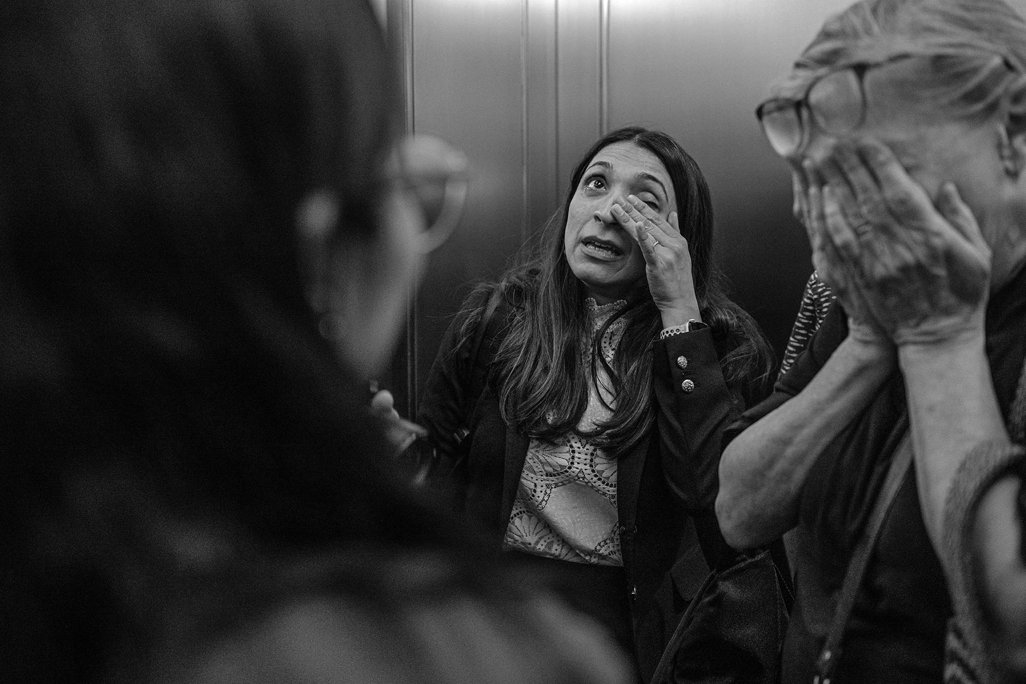 Two women wipe tears from their faces in an elevator.