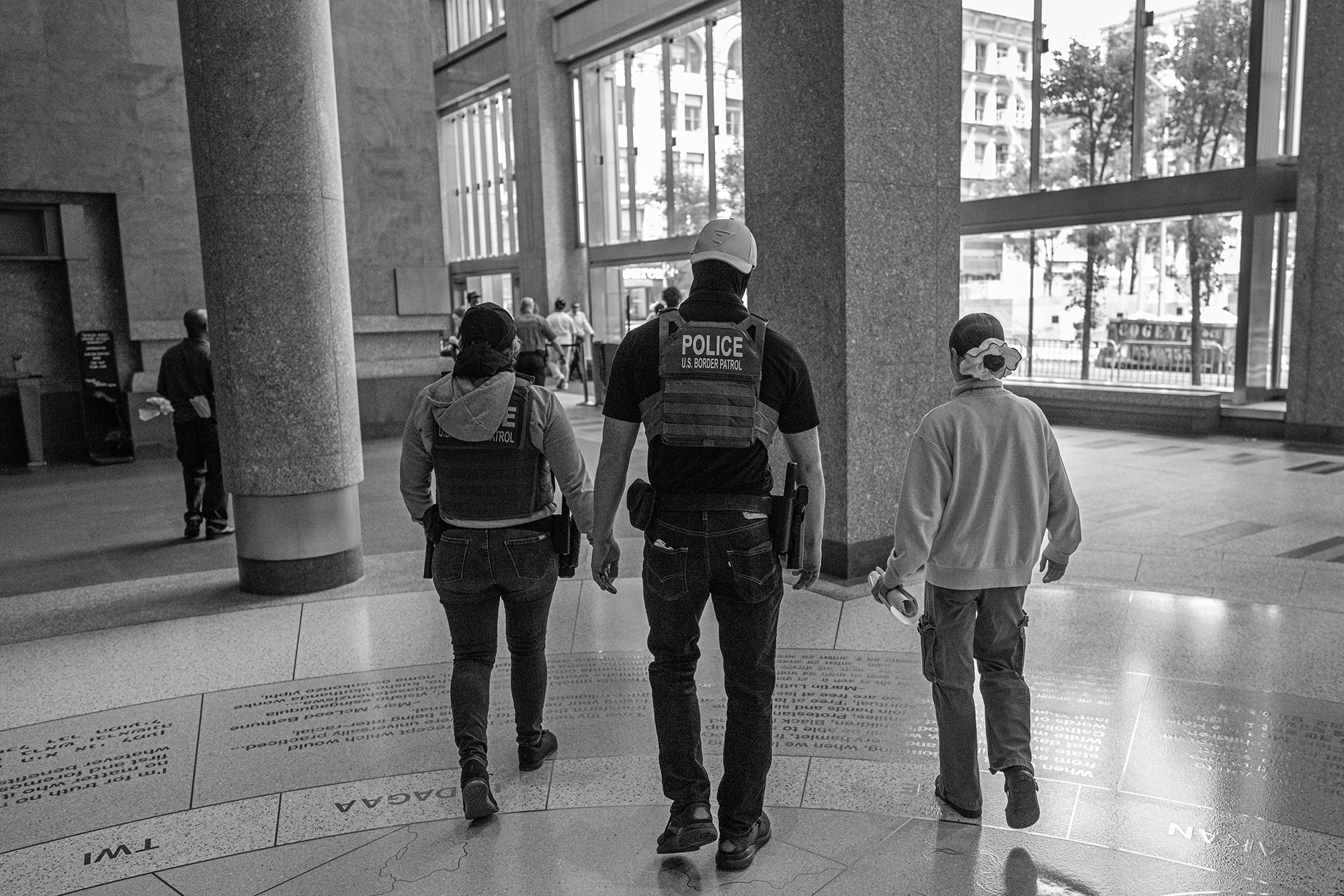 US Border Patrol agent walk with two people on either side of him.