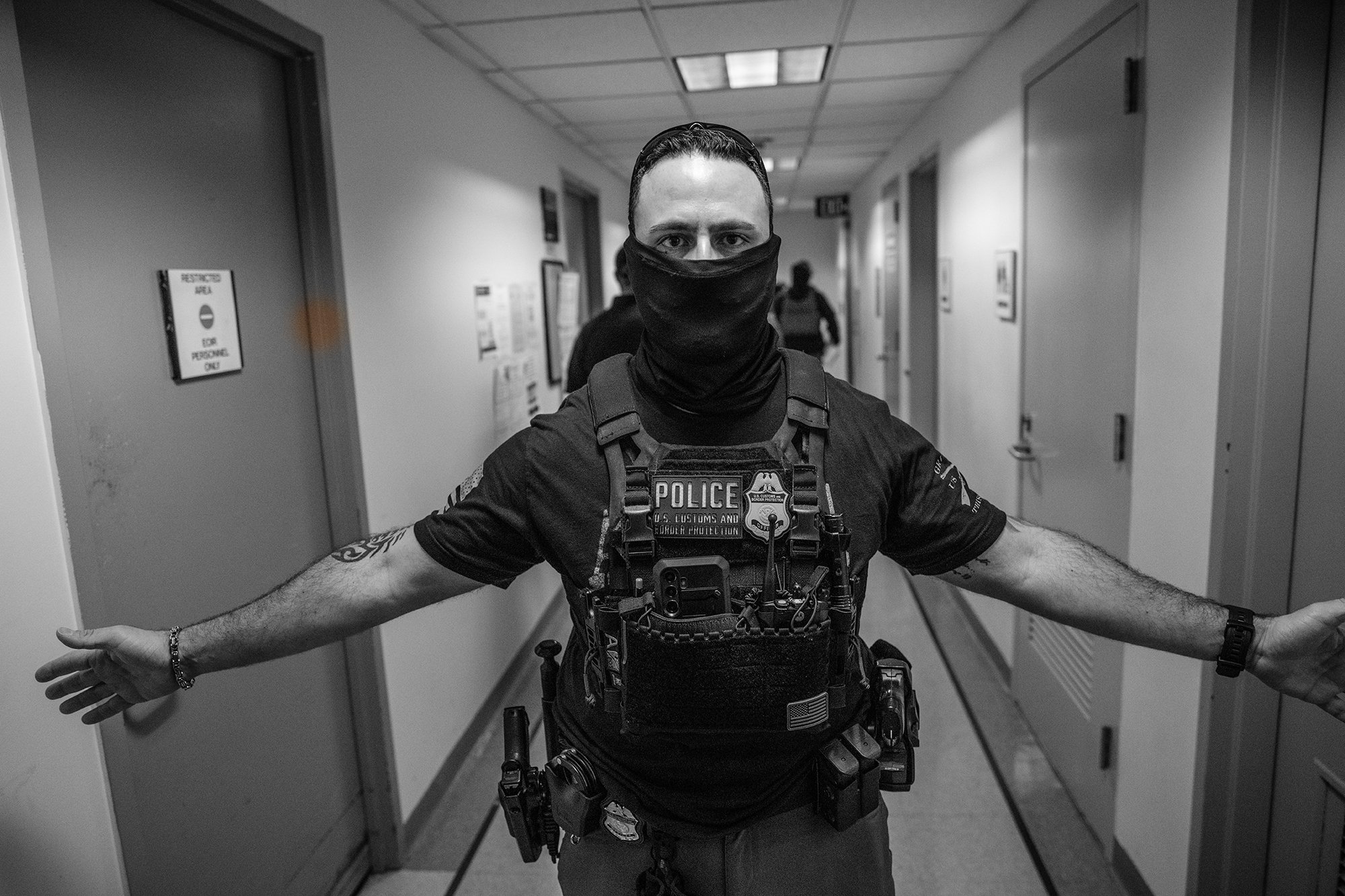 Masked federal agents has his arms spread blocking access to a hallway.