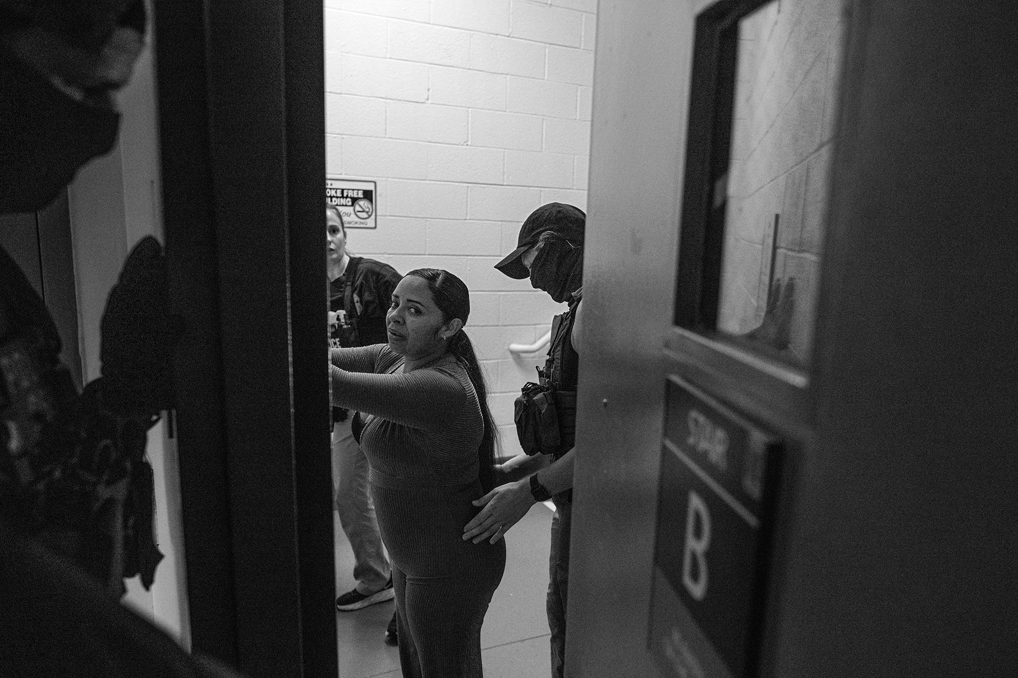 Woman being detained looks through a doorway that is being closed.