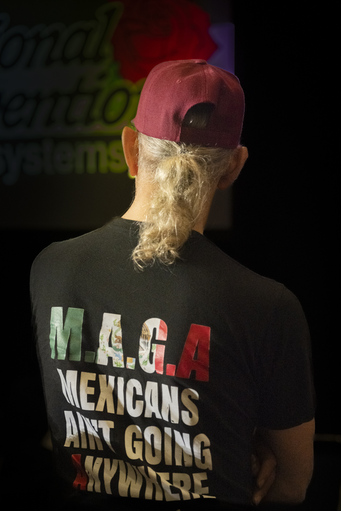 Portrait of back of man wearing shirt that reads, "MAGA: Mexicans Ain't Going Anywhere."