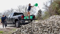 A person throws dried oysters into a large pile from a truck bed.
