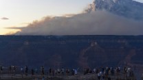 A scene of dozens of people looking out over the Grand Canyon with smoke billowing in the distance.