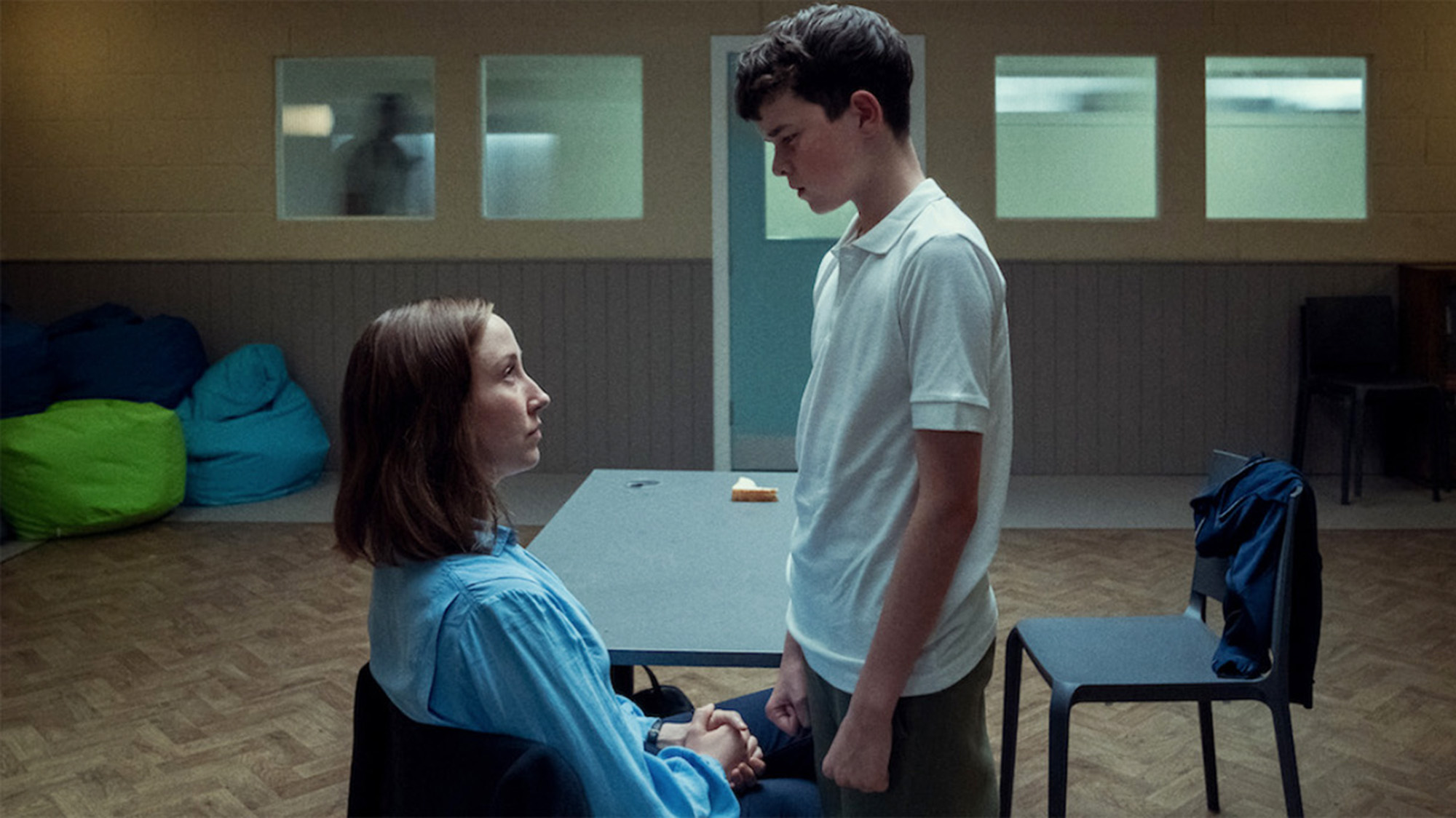 Young boy standing over a woman sitting in a chair; still from TV show "Adolescence."