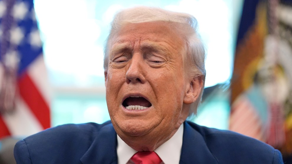 A close-up photo of Donald Trump with his eyes partially closed, eyebrows furrowed, and mouth open in a strained expression, as if wincing or shouting. He is wearing a dark blue suit, white shirt, and red tie. The background is blurred but shows American flags and the presidential seal, suggesting the picture was taken inside the Oval Office.