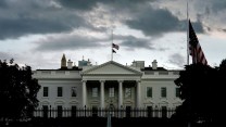Front view of the White House, with flags at half-staff, under a cloudy and ominous sky.