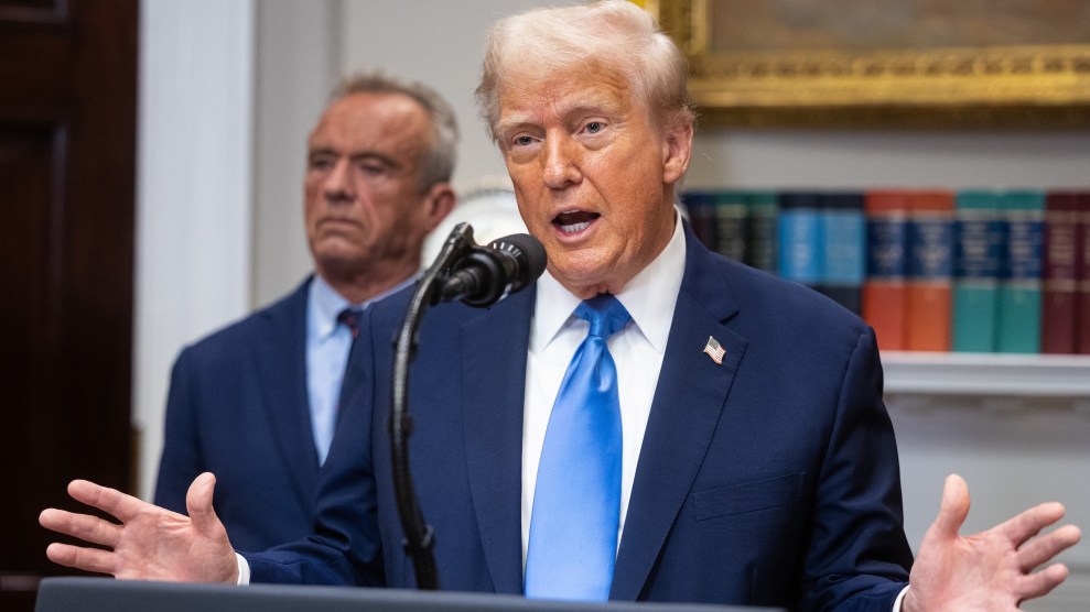 Donald Trump speaking at a podium waving his hands with Robert F. Kennedy Jr standing behind him.