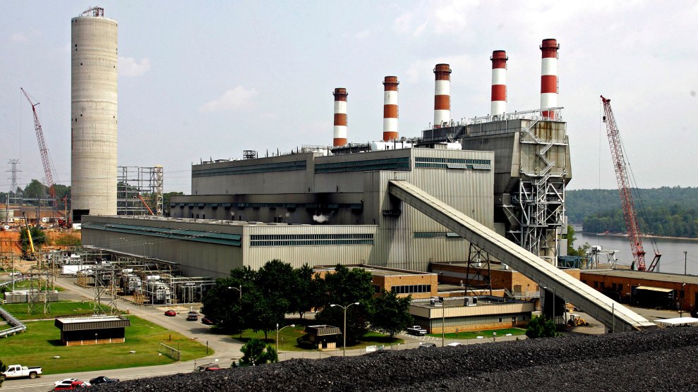 A large power plant with five candy-striped smokestacks and a long coal elevator extending into a giant coal pile in the foreground.